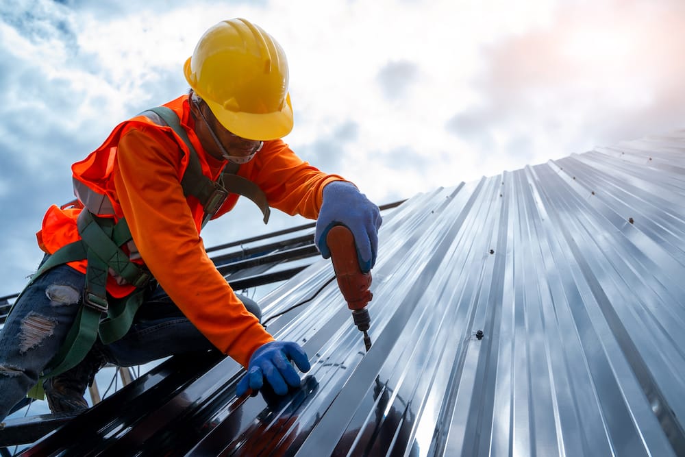 Roofer in protective uniform wear use electric drill to install the metal sheet on the new roof